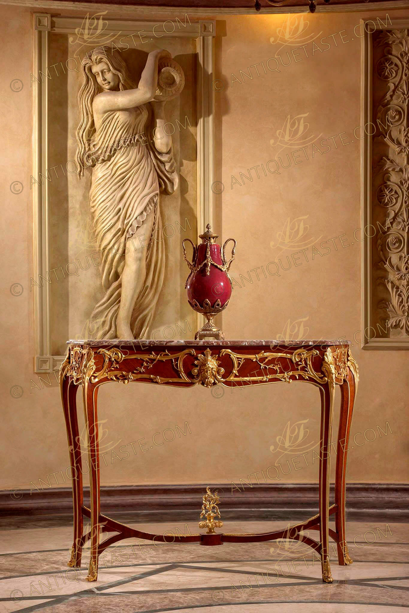 A prodigious French 19th Century Belle Époque Louis XV Rococo style gilt-ormolu-mounted freestanding Console Table after the model by François Linke, The beveled marble top of serpentine outline above an undulating frieze centered by a finely chased ormolu  female mask with acanthus leaves headdress and foliage volutes within C-scroll and leafy encadrements repeated on the sides; Raised on angular cabriole legs surmounted by large acanthus leaves chutes, bordered with ormolu trim and ending in foliate scroll sabots, joined by an ormolu mounted inverted curved double X stretcher centered by a platform surmounted by a finial of an urn of prosperity surmounted by scrolling leaves, The original console table, with a mandolin player centering the stretcher and rococo acanthus mounts, although designed in the Louis XV style, is not fully developed in combining this style with the Art Nouveau style for which François Linke is renowned. Linke drew his inspiration from the extravagant Rococo creations of François de Cuvilliés (1695-1968) that can be seen in the engravings of Johann Michael Hoppenhaut in the 1750's